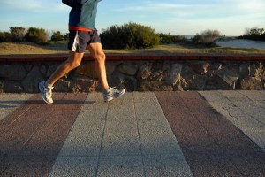 Young male athlete jogging at the promenade. Legs in motion. A quiet beach with sand dunes on the background