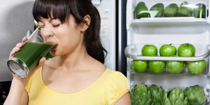 Grimacing mixed race woman drinking healthy drink near refrigerator